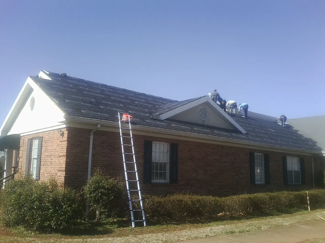 Crew tearing shingles off a brick ranch roof with a ladder set — Emergency Roof Repair work by our crew in Vale