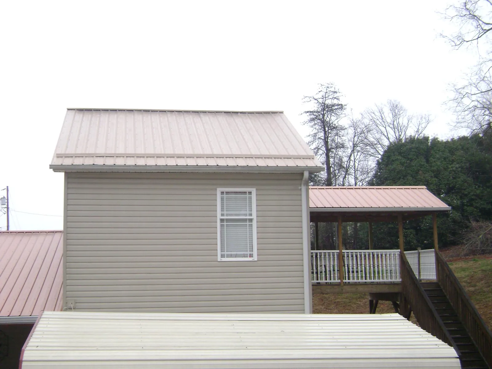 Tan metal roofs on a two story addition and attached porch, from a Roof Replacement job in Vale
